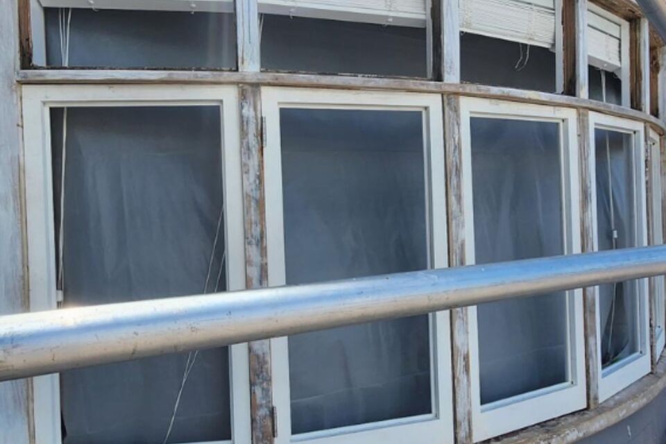 A large curved wooden window frame with peeling paint and weathered timber, showing signs of deterioration. The aging windows are prime candidates for restoration and retrofit double glazing. The Glaziers Ltd in Auckland specialises in upgrading timber windows with energy-efficient double glazing, enhancing insulation while preserving the home's original character.